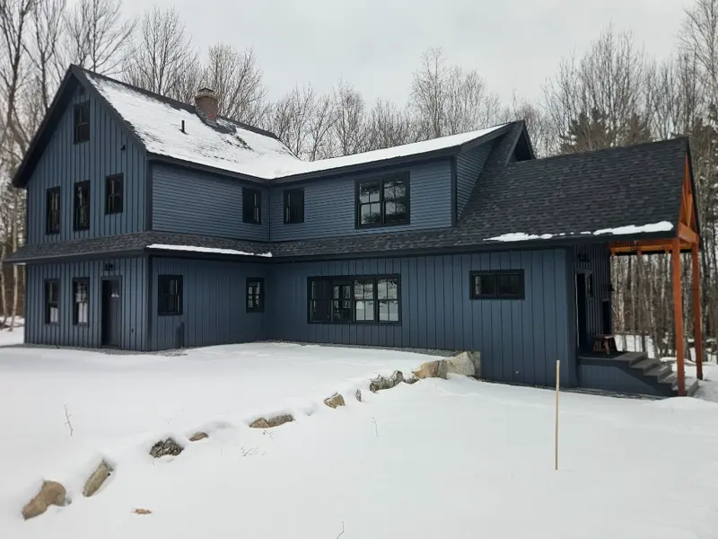 Full exterior view of a custom-built blue farmhouse with timber accents in the snow
